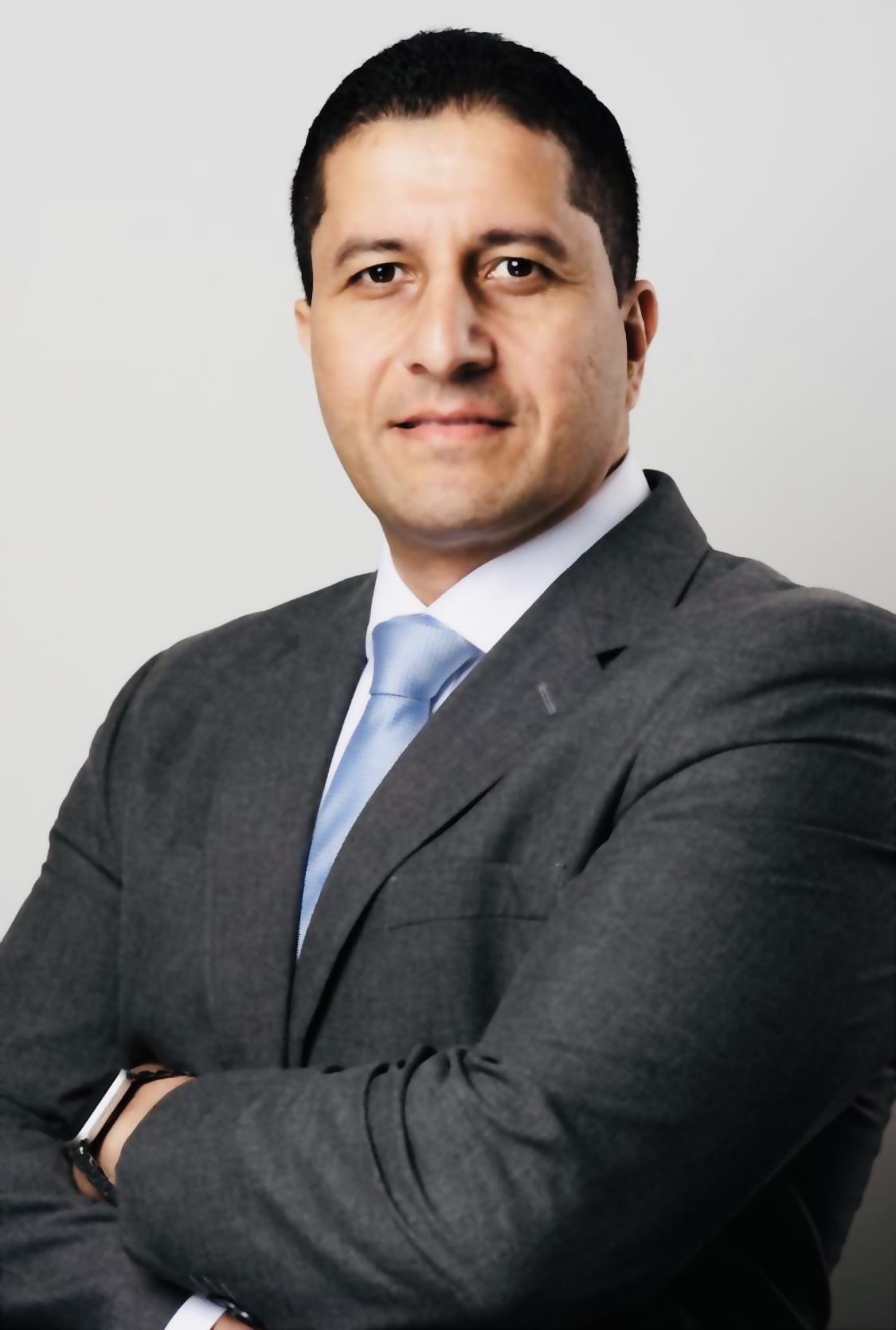 Portrait photo of Dr Naz, wearing a dark suit, white shirt and blue tie.