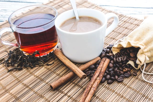A cup of coffee and a cup of tea with coffee beans and tea leaves