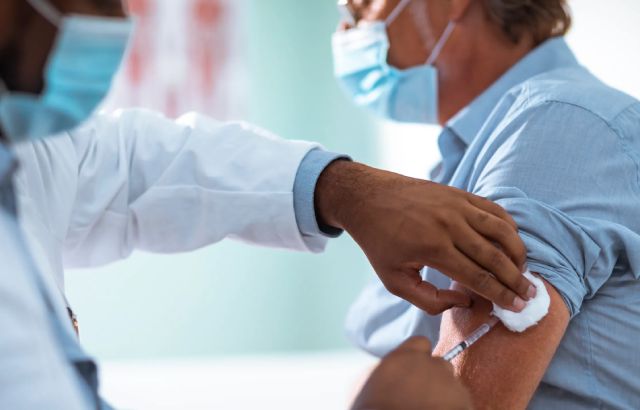 A man wearing a face mask is injected in his left arm with a hypodermic needle