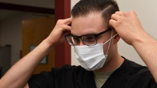 A person in glasses putting on a face-mask