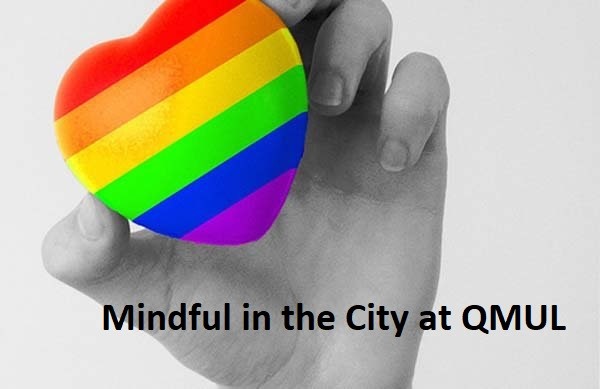A black and white image of a hand holding a rainbow coloured heart. Overlaid with text reading 'Mindfulness in the City at Queen Mary'